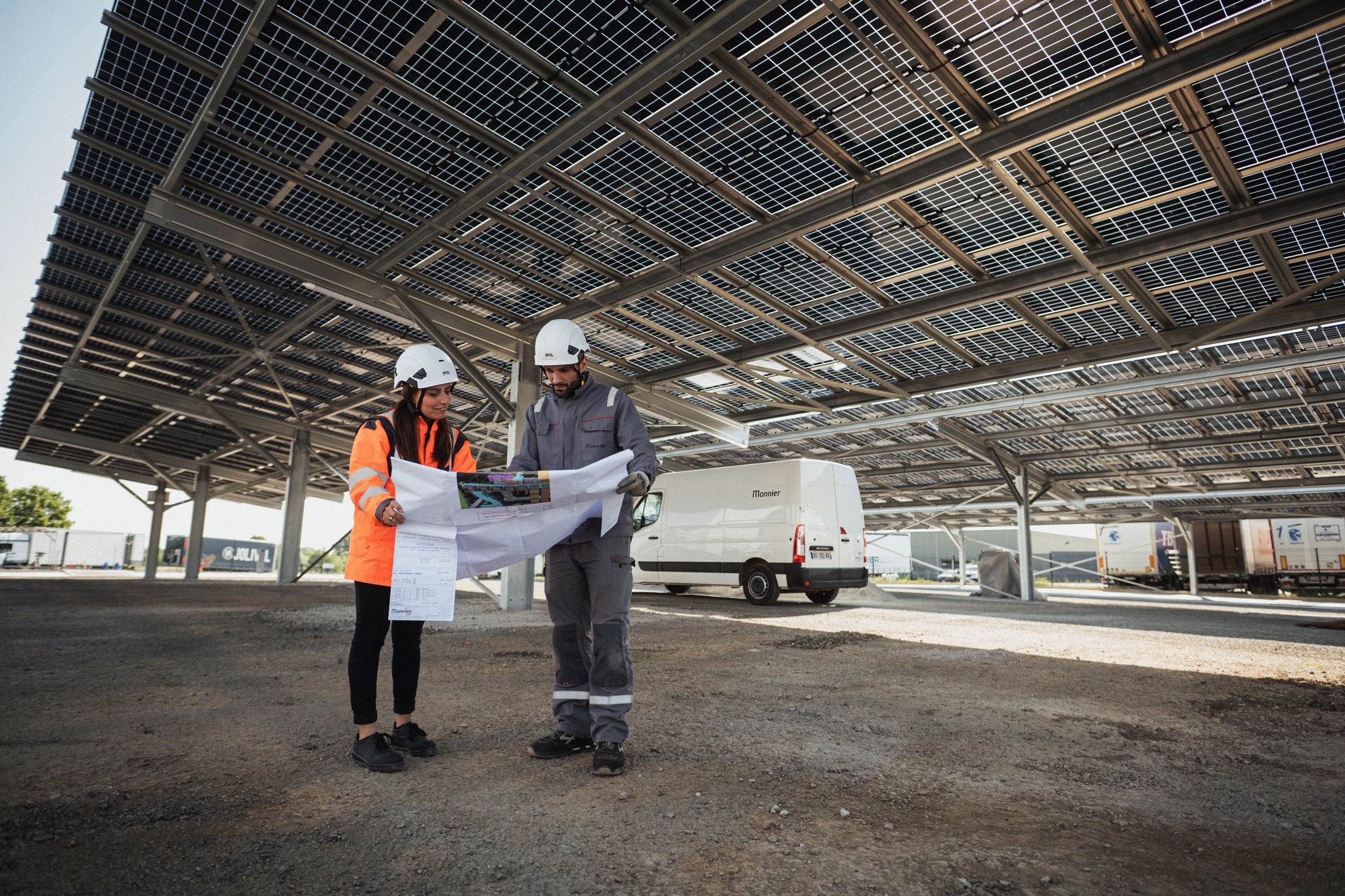 Photo de deux techniciens regardant un plan sous une ombrière photovoltaïque