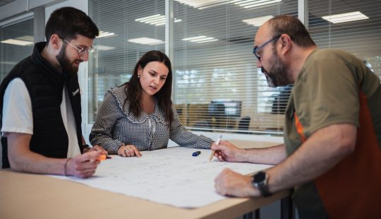 Photo de trois personnes devant un plan électrique