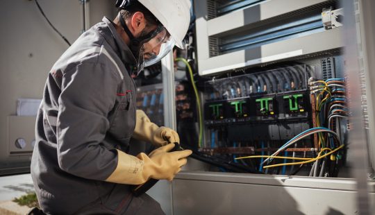 Photo d'un ouvrir en tenue de sécurité devant un tableau électrique ouvert